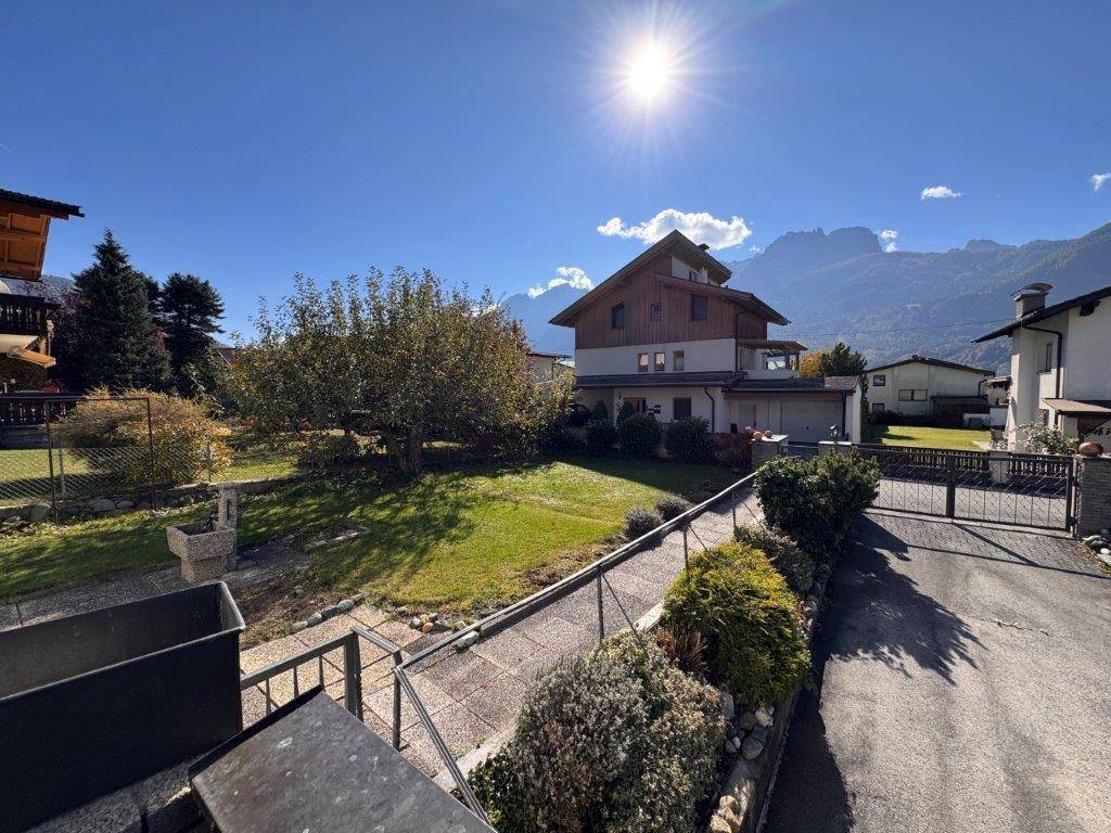 Sonniger Gartenbereich mit Haus, Zufahrt und beeindruckendem Panoramablick auf die Berge.