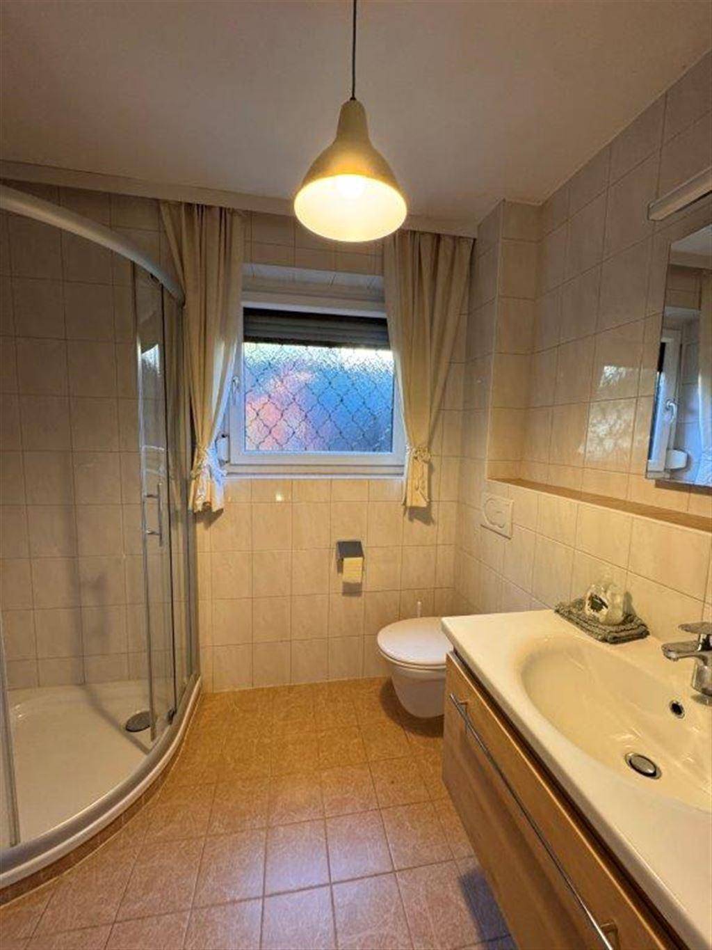 Helles Badezimmer mit Duschkabine, Waschtisch, Toilette und Fenster.