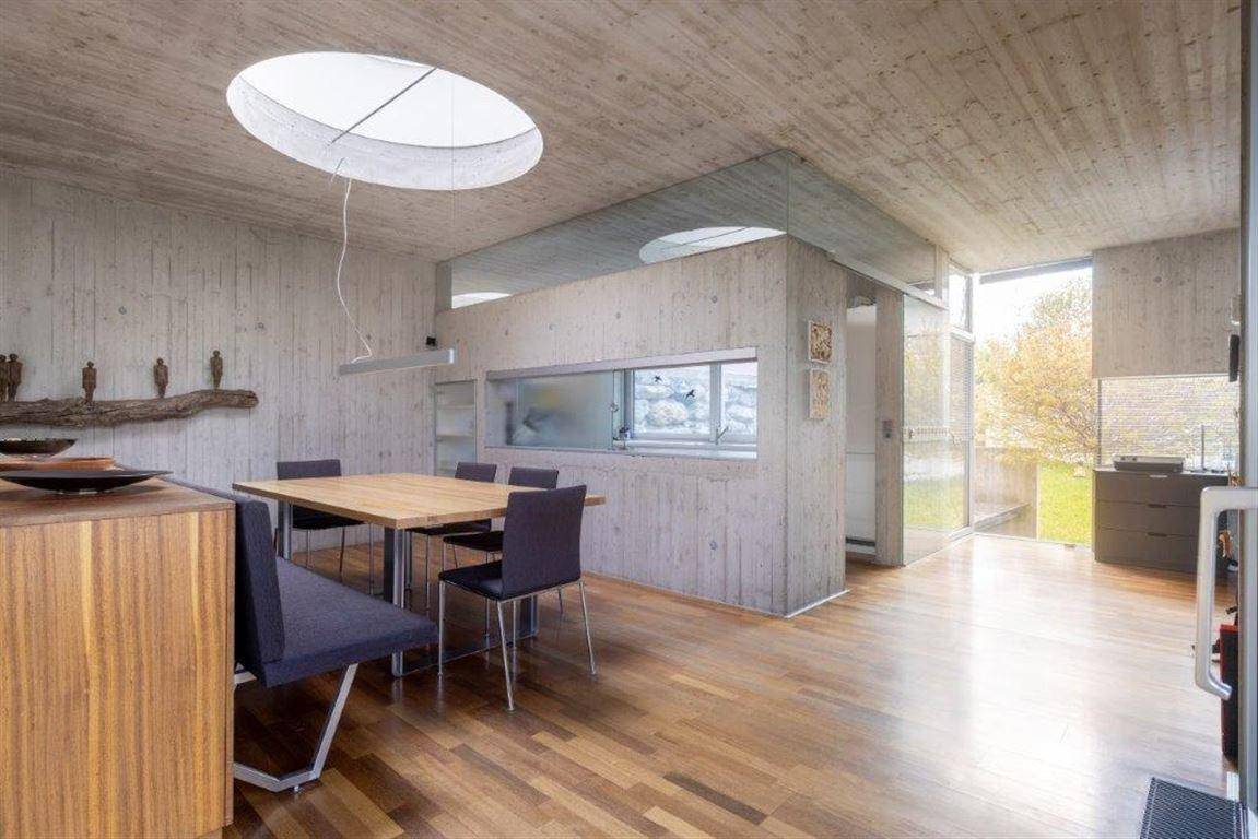 Essbereich mit Holztisch, modernen Stühlen, Oberlicht und Sichtbetonwänden.
