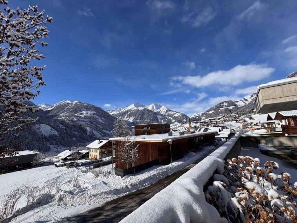 Winterliche Ansicht der Siedlung mit schneebedeckten Dächern und majestätischen Bergen im Hintergrund.