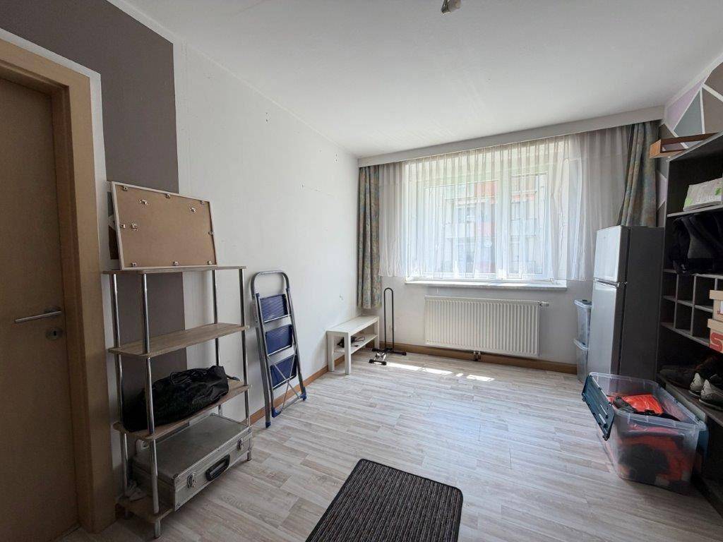 Leeres Zimmer mit Laminatboden, großem Fenster und Heizkörper.