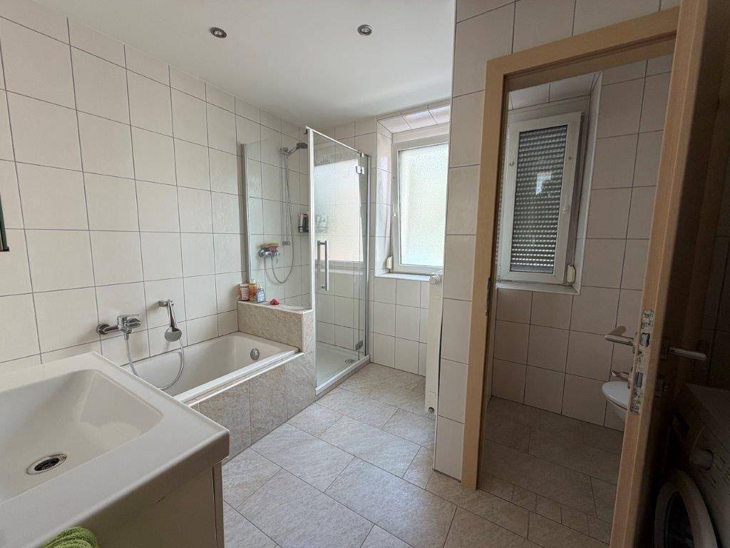 Helles Badezimmer mit Badewanne, Duschkabine, Waschbecken und Fenster.