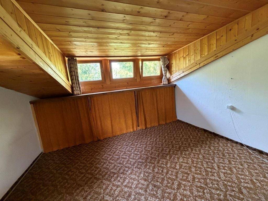 Gemütliches Dachzimmer mit Holzverkleidung, Teppichboden und mehreren Fenstern für Tageslicht.