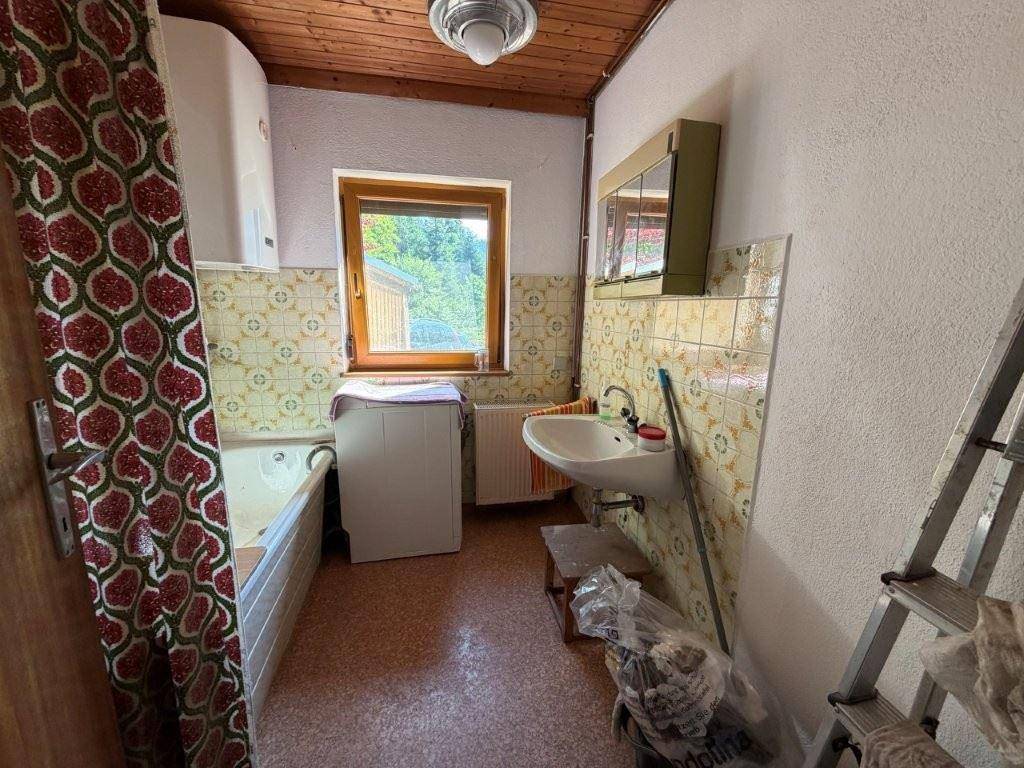 Badezimmer mit Badewanne, Waschbecken, Fenster und gemusterten Fliesen im 80er-Jahre-Stil.