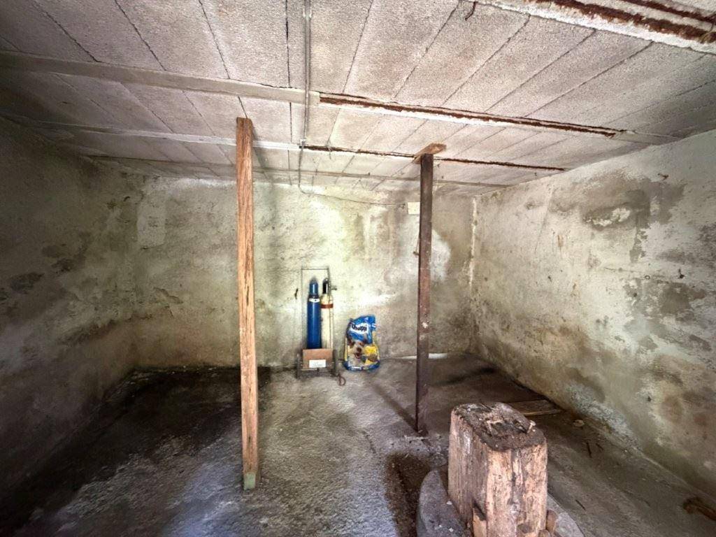 Unfertiger Kellerraum mit Betonwänden, Decke und Holzstützbalken, als Lagerraum genutzt.