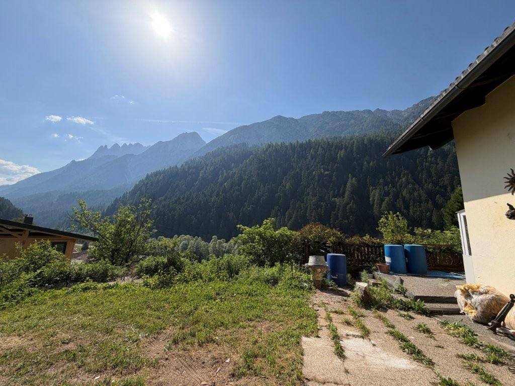 Sonniger Gartenbereich mit weitem Blick auf die umliegende Berglandschaft und dichte Wälder.