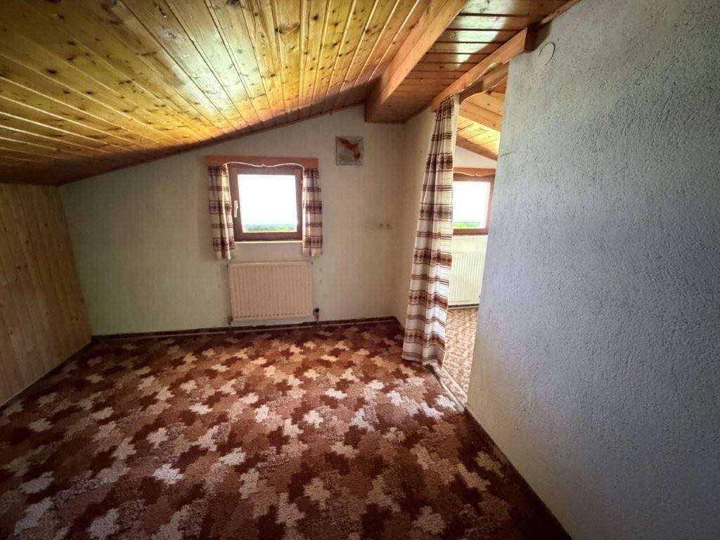 Dachzimmer mit schräger Holzdecke, gemustertem Teppichboden und kleinem Fenster mit Bergblick.