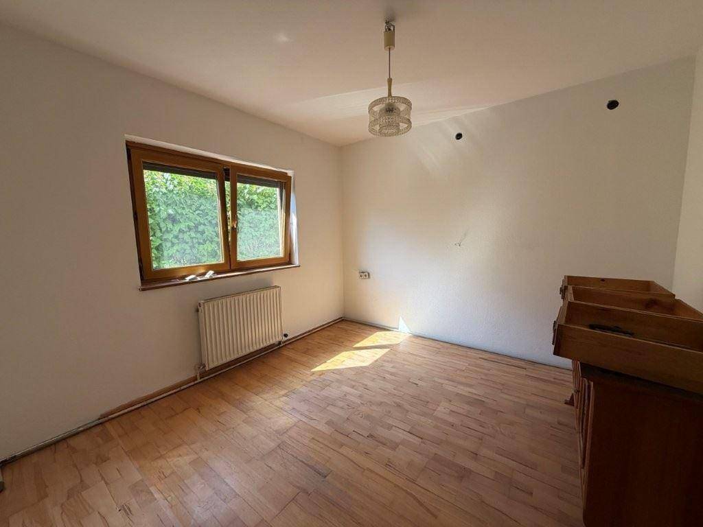Helles Zimmer mit Holzboden, weißen Wänden und Fenster mit Blick ins Grüne.