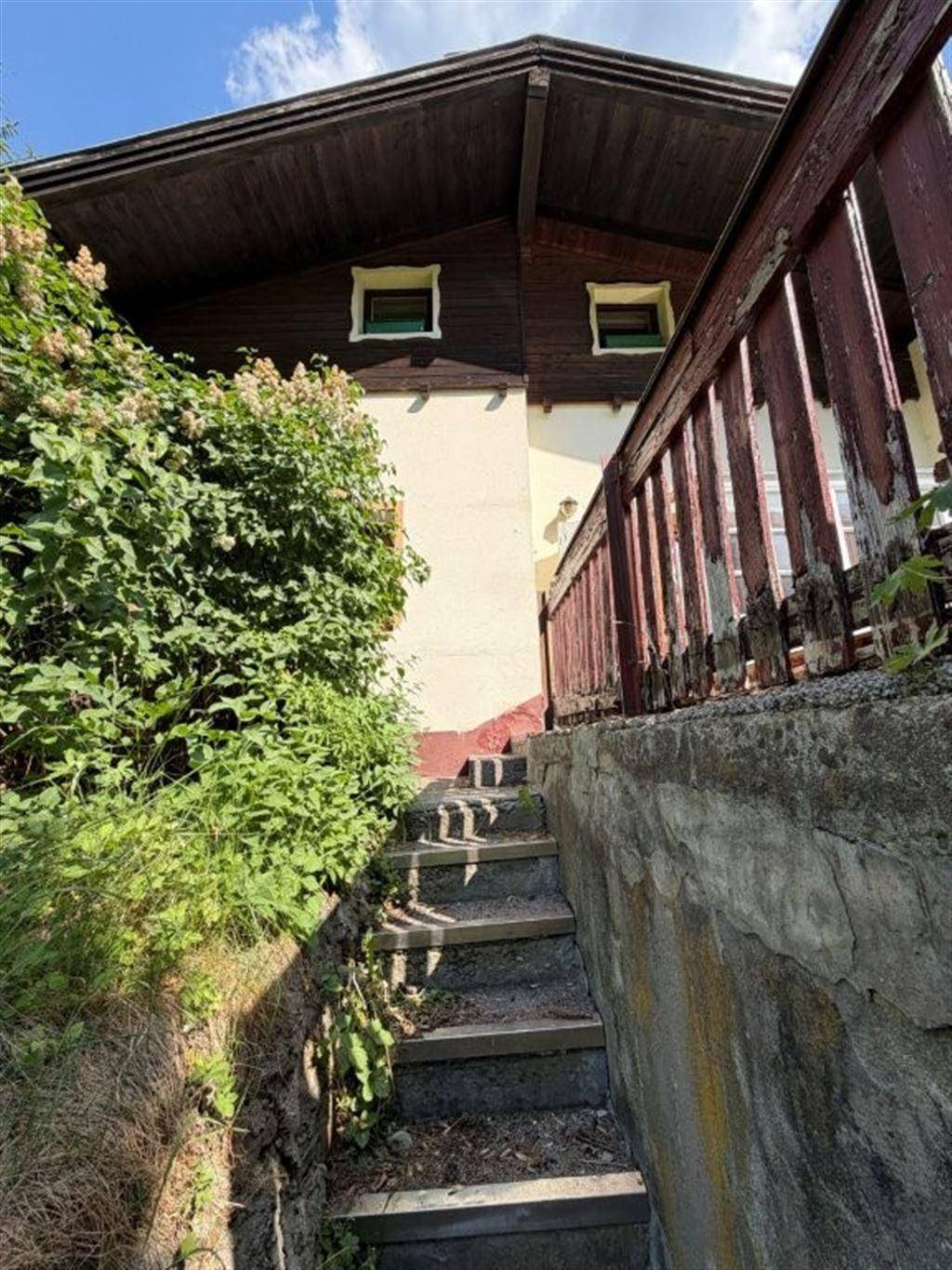 Steintreppe führt zum Eingang des Hauses, umgeben von üppiger Vegetation und Bäumen.