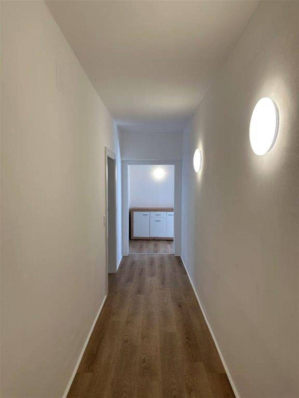 Langer, heller Flur mit Laminatboden und modernen Wandleuchten.