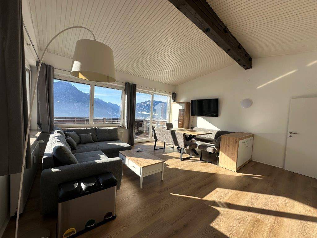 Helles Wohn- und Esszimmer mit gemütlichem Sofa, Holzboden und Panoramablick auf die verschneiten Berge.
