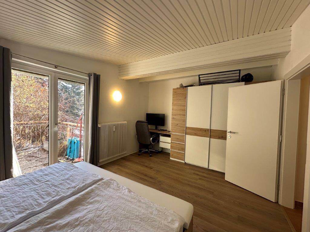 Schlafzimmer mit Doppelbett, Kleiderschrank, Schreibtisch und Zugang zum Balkon.
