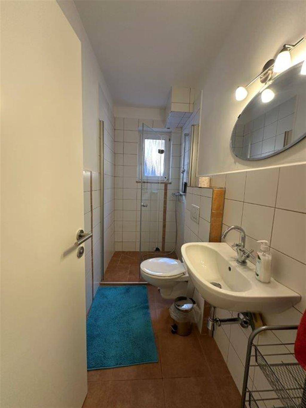 Kleines Badezimmer mit Dusche, WC, Waschbecken und einem Fenster für Tageslicht.