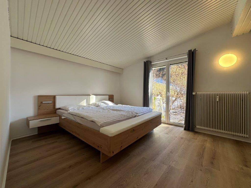 Schlafzimmer mit Holzbett, Laminatboden und direktem Zugang zu einem Außenbereich.