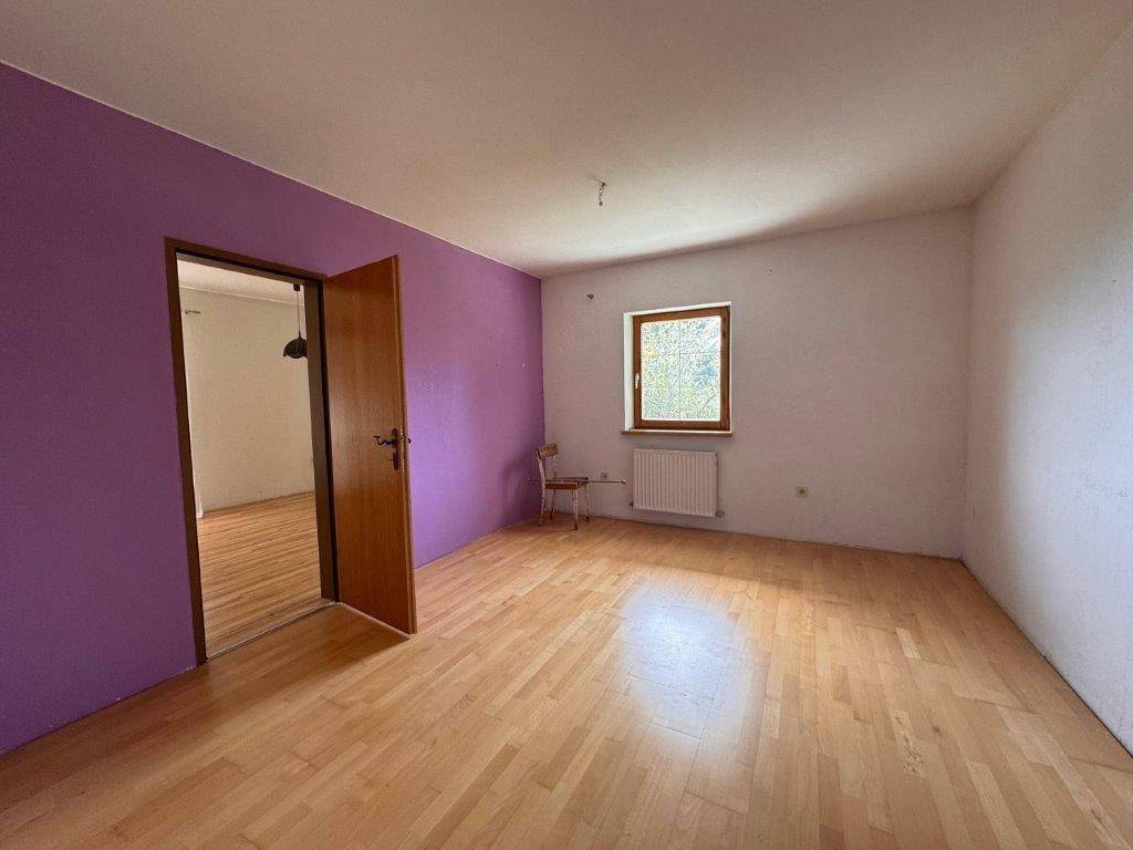 Helles Zimmer mit Holzboden und einer lila Akzentwand, bereit zur individuellen Gestaltung.