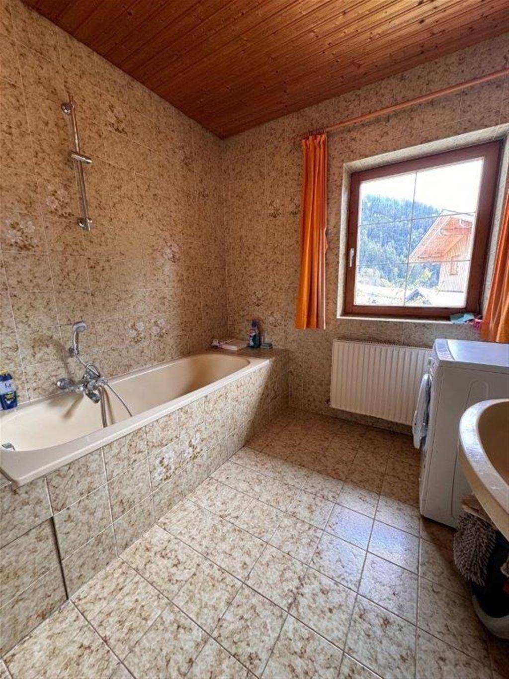 Gefliestes Badezimmer mit Badewanne, Fenster und Waschmaschine, bietet Bergblick.
