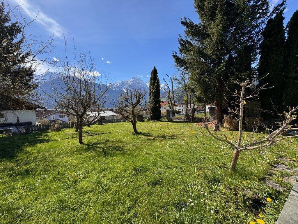 Gepflegter Garten mit Rasenfläche und Obstbäumen, umgeben von einer beeindruckenden Bergkulisse.