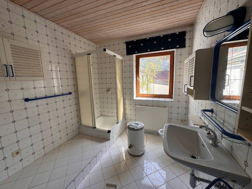Helles Badezimmer mit weiß-blauen Fliesen, Duschkabine und Fenster, bietet viel Tageslicht.