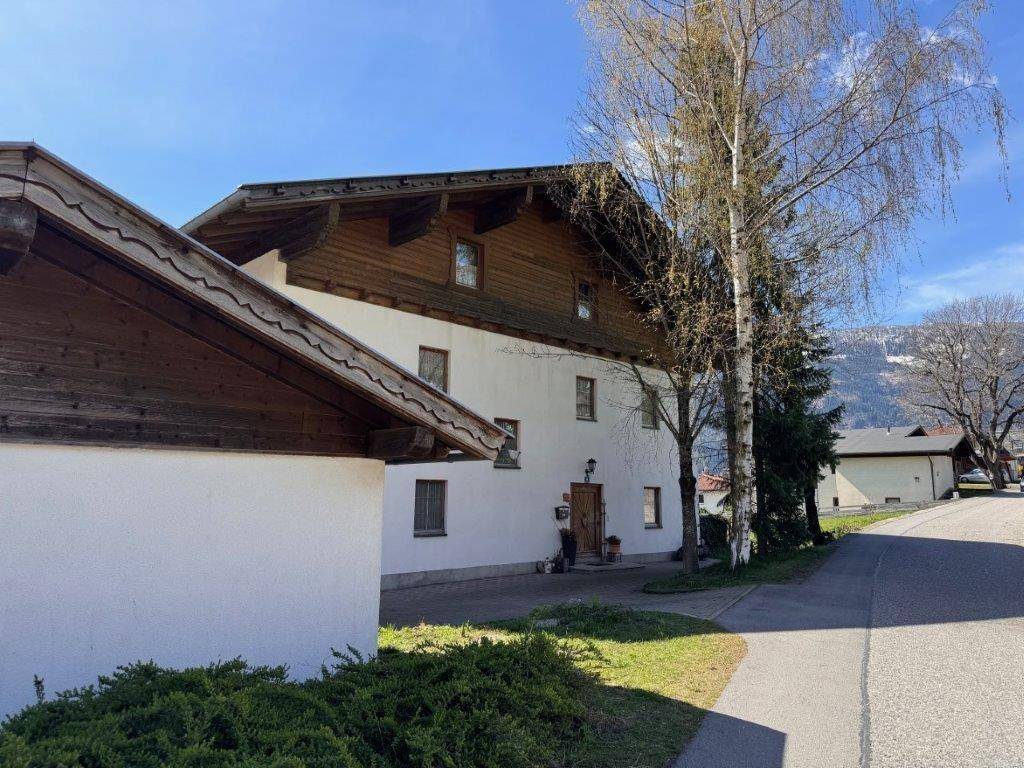 Ansicht des Hauses von der Straße mit gepflegter Fassade und Zufahrt, umgeben von Bäumen.