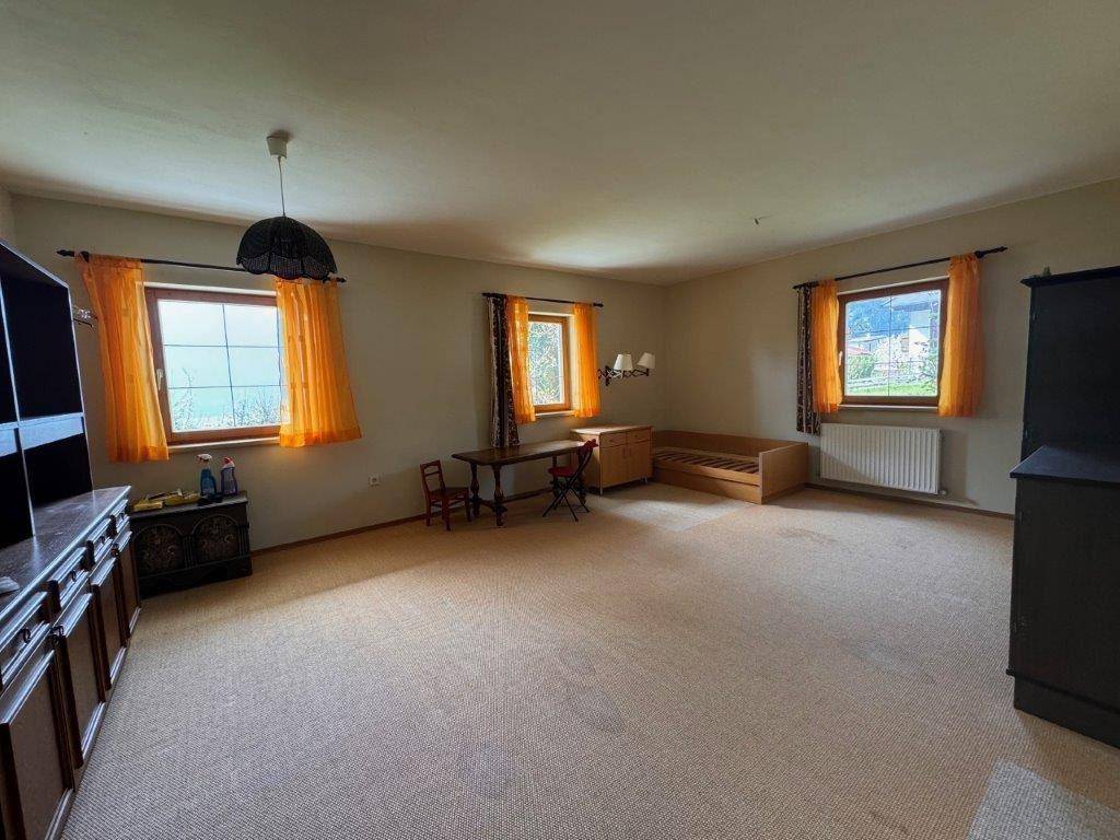 Geräumiges Wohnzimmer mit Teppichboden und mehreren Fenstern, die viel Licht hereinlassen.