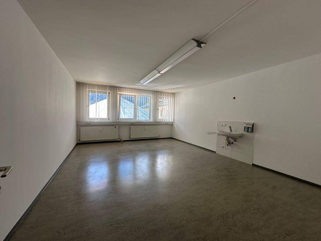Geräumiger Büroraum mit Linoleumboden, Waschbecken und großen Fenstern mit Jalousien.