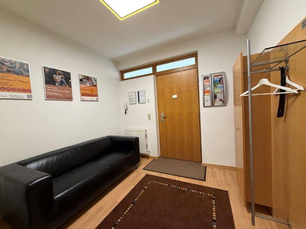 Empfangsbereich mit schwarzem Ledersofa, Holzboden und Garderobe neben der Eingangstür.