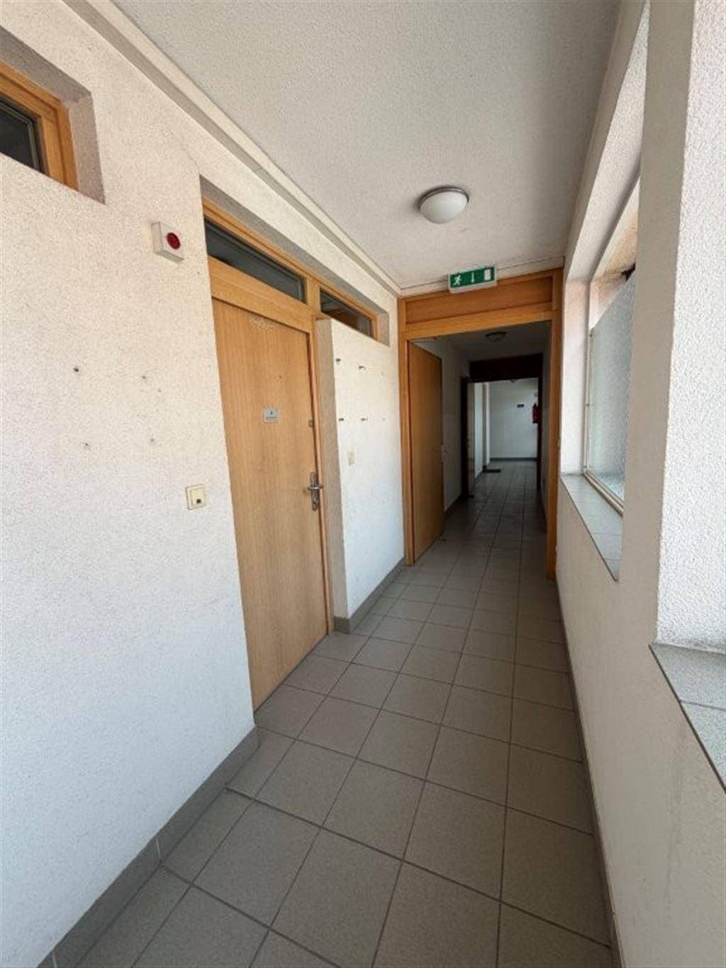 Langer Flur mit Fliesenboden, Holztüren und Fenstern, die Tageslicht hereinlassen.