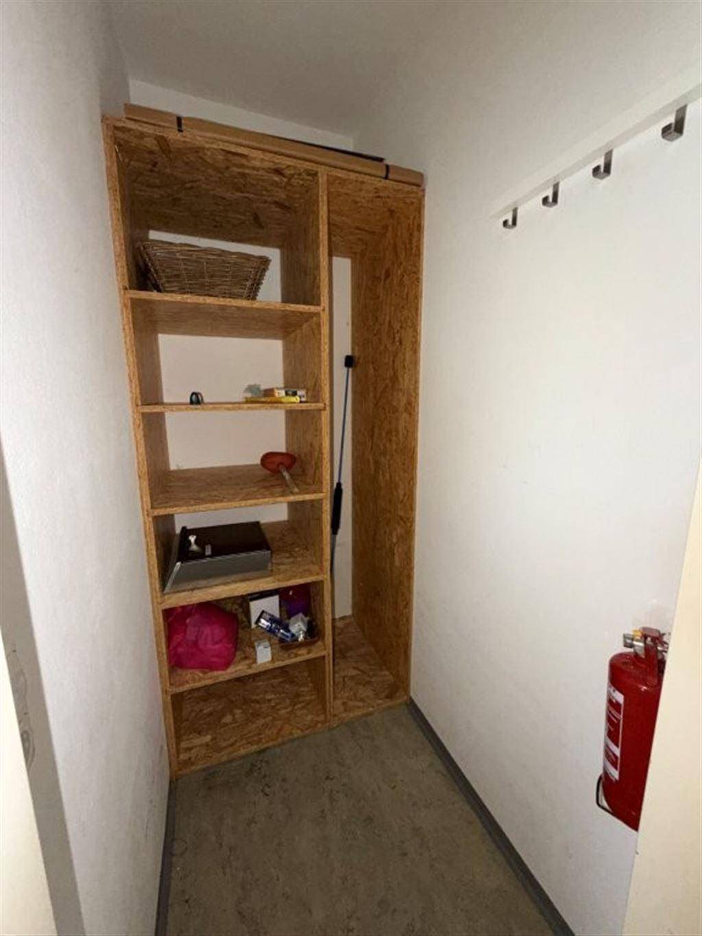 Kleiner Abstellraum mit Holzregalen und einem Feuerlöscher an der Wand.