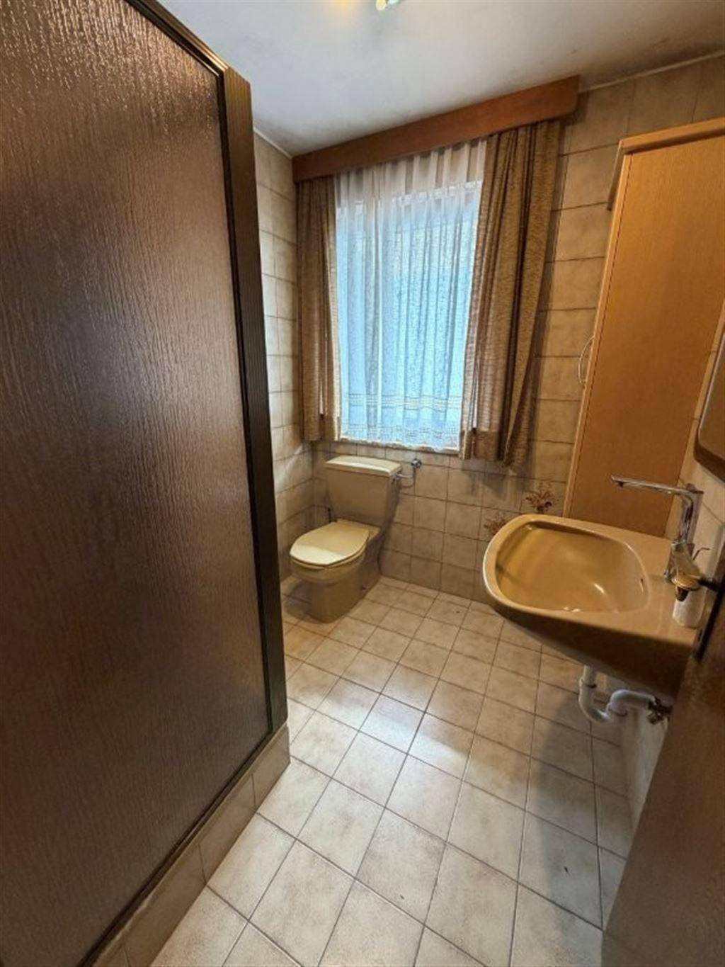 Badezimmer mit WC, Waschbecken und Fenster, ausgestattet im Stil der 80er Jahre.