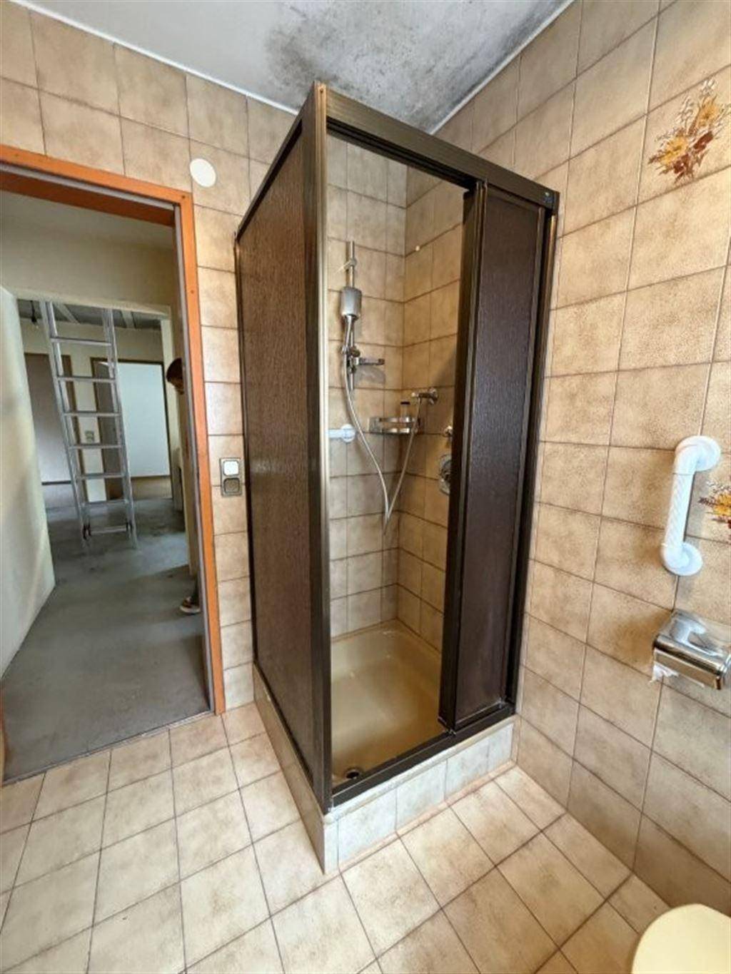Badezimmer mit Duschkabine, Fliesenboden und Wandfliesen im 80er-Jahre-Stil.