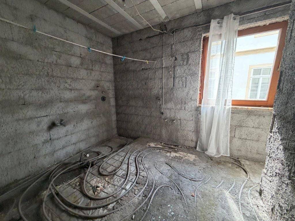 Raum im Rohbau mit sichtbaren Leitungen für Fußbodenheizung und einem Fenster.