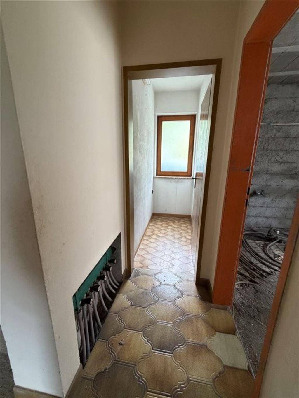 Flur mit Fliesenboden und sichtbaren Leitungen, der zu einem Raum im Rohbau führt.