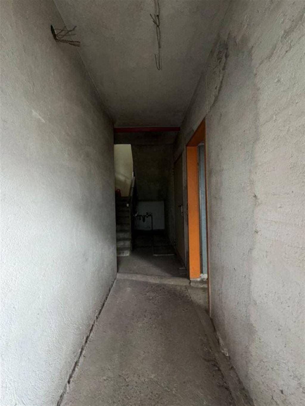 Unfertiger Flur im Rohbau mit Betonwänden und Treppenaufgang im Hintergrund.