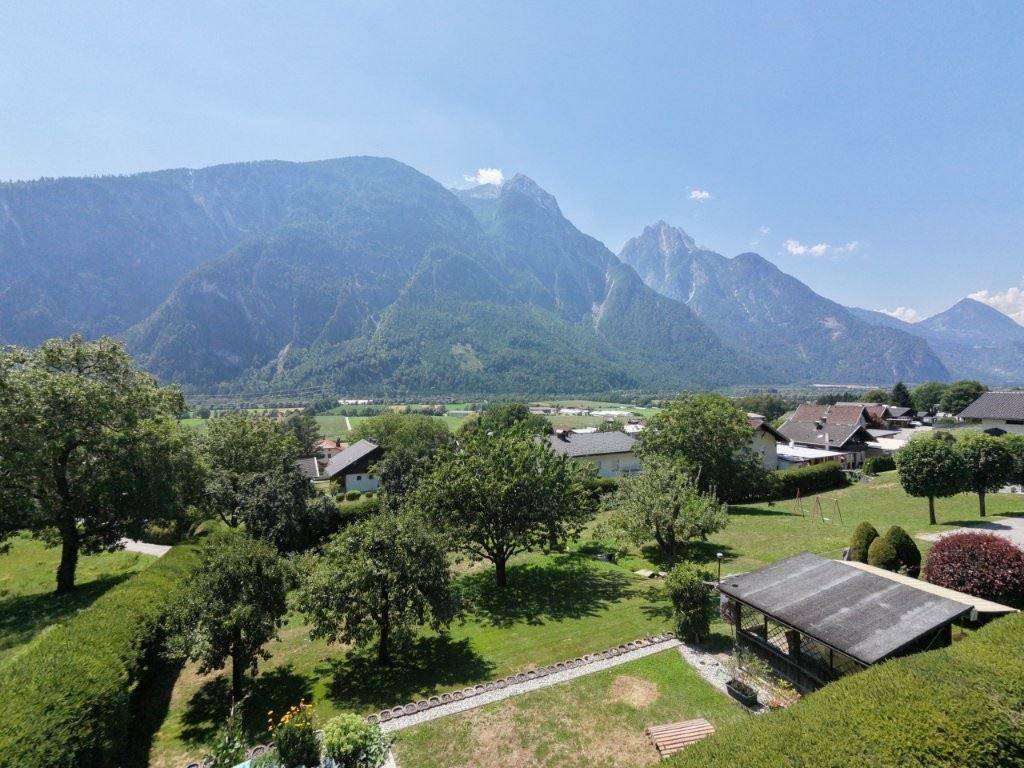 Panoramablick auf die grüne Landschaft mit Häusern, Gärten und beeindruckenden Bergen im Hintergrund.