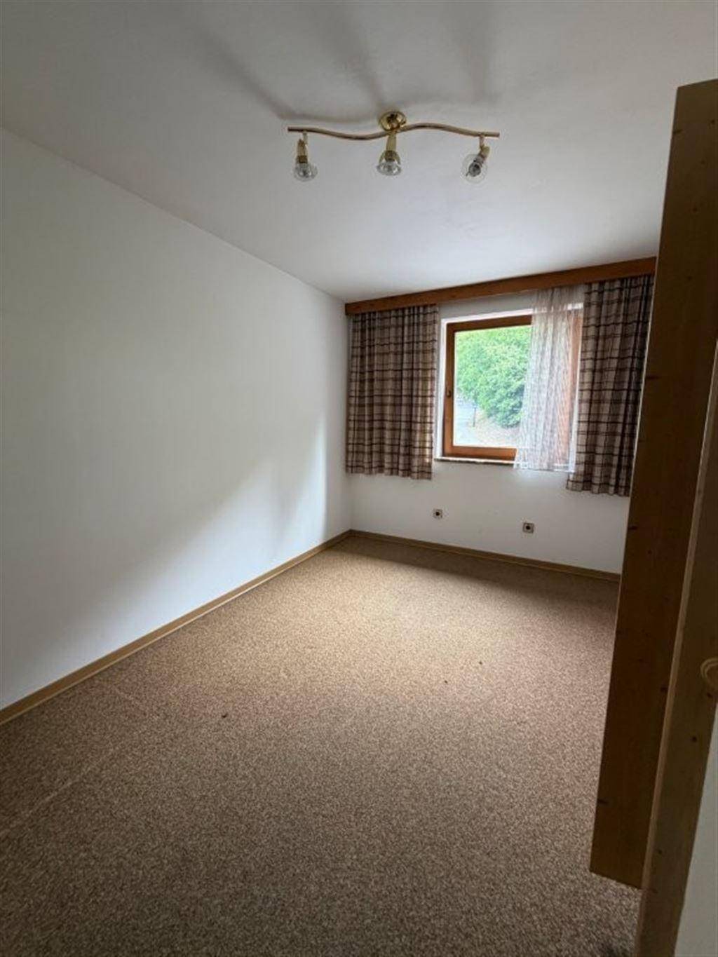 Schlafzimmer mit Teppichboden, Fenster und neutralen Wänden, bereit zur Einrichtung.