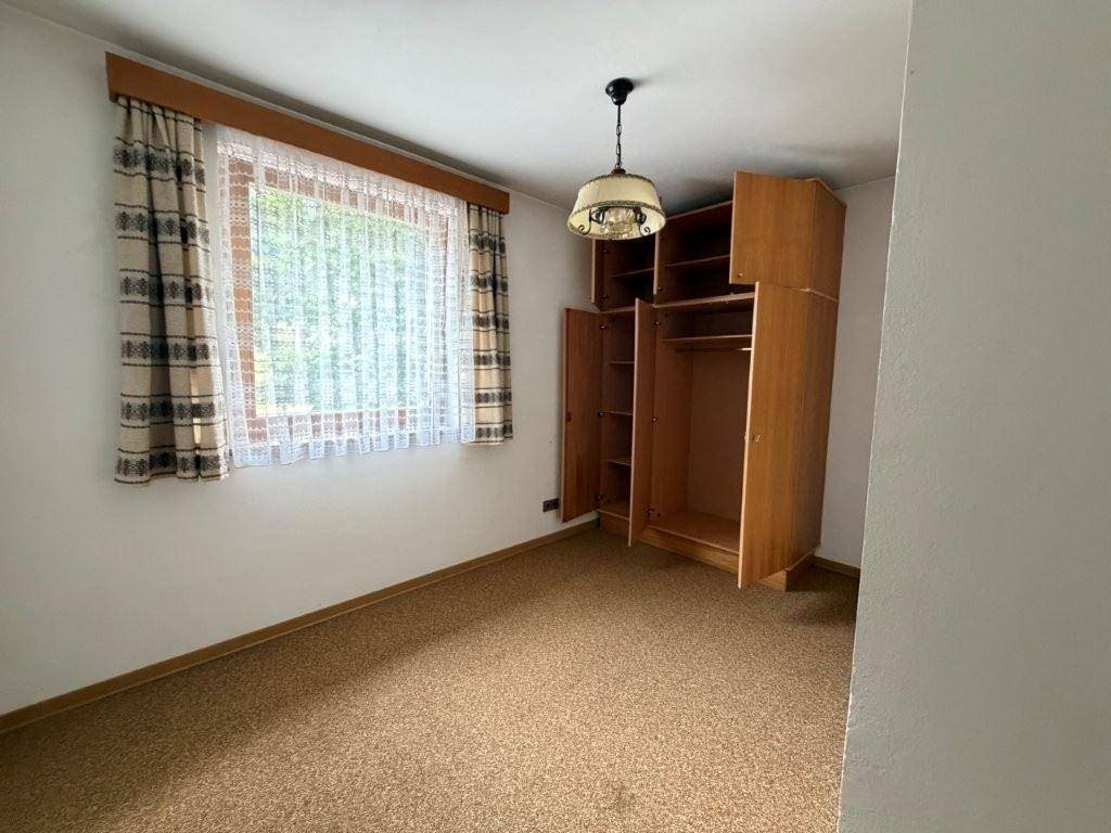 Schlafzimmer mit Teppichboden, Fenster und einem offenen Holzschrank.