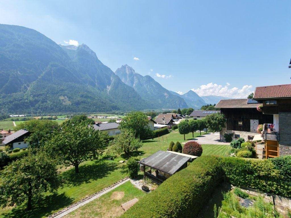 Malerischer Ausblick auf die Berglandschaft mit ländlichen Häusern und gepflegten Gärten unter blauem Himmel.