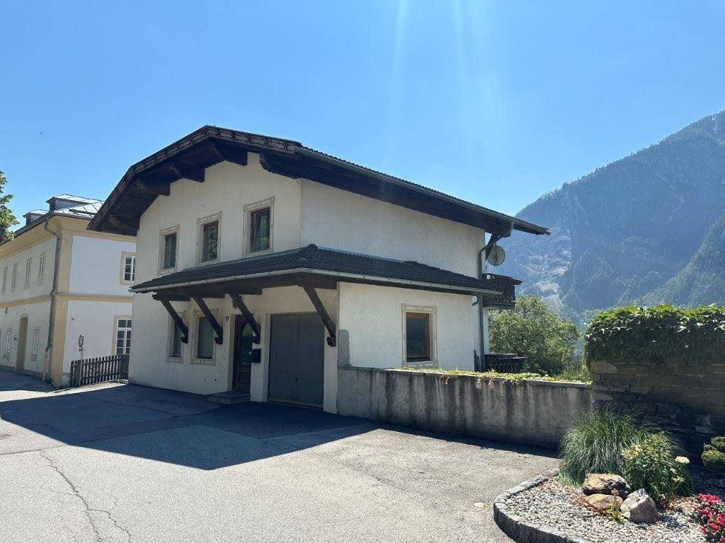 Seitenansicht des traditionellen Hauses mit Garage, gepflegtem Vorgarten und Blick auf die Berge.