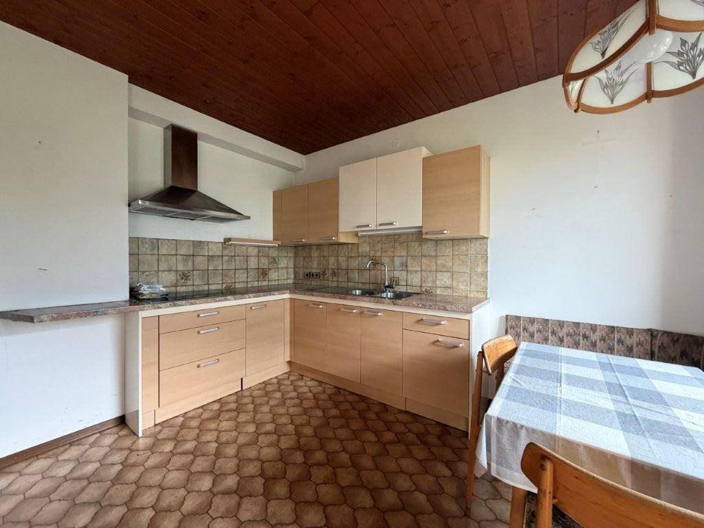 Einbauküche mit hellen Holzfronten, Fliesenboden und Essbereich mit karierter Tischdecke.