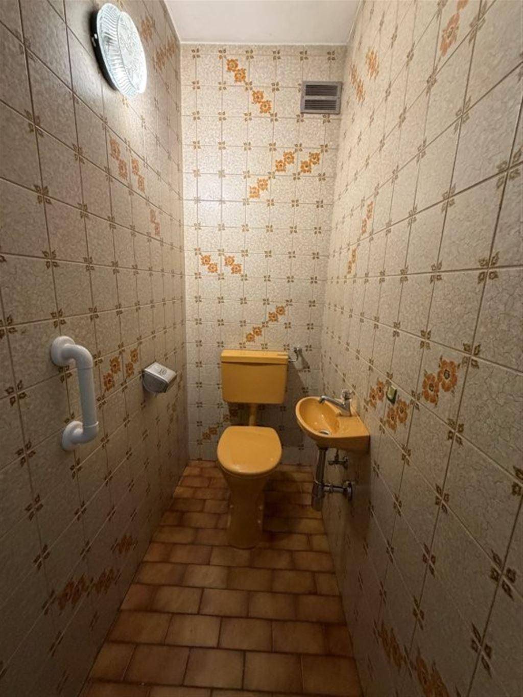 Kleines WC mit gelber Toilette, Waschbecken und auffälligen Wandfliesen im Retro-Stil.
