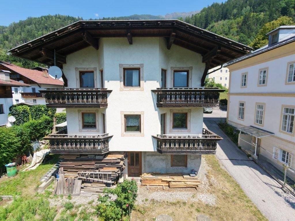 Traditionelles Haus mit mehreren Holzbalkonen und einem Satteldach, umgeben von grüner Natur und Bergen.
