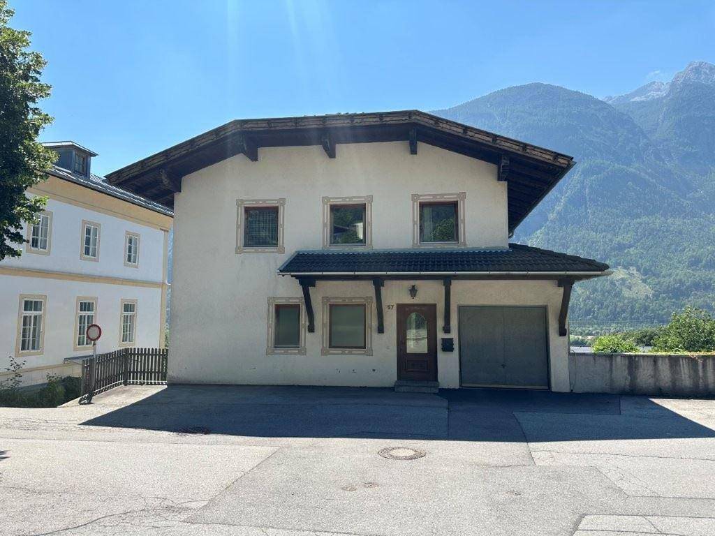 Vorderansicht eines traditionellen Hauses mit integrierter Garage und Bergblick an einem sonnigen Tag.