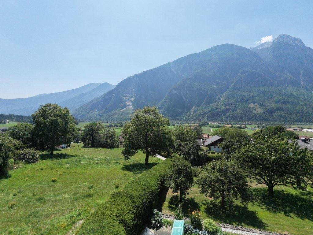 Weitläufige grüne Landschaft mit Bäumen und majestätischen Bergen im Hintergrund unter blauem Himmel.