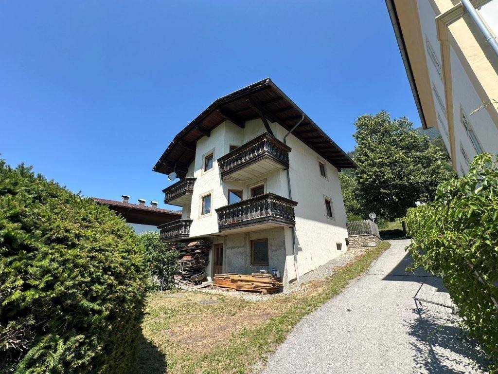 Seitenansicht des traditionellen Hauses mit mehreren Holzbalkonen und einem Weg, umgeben von grüner Natur.