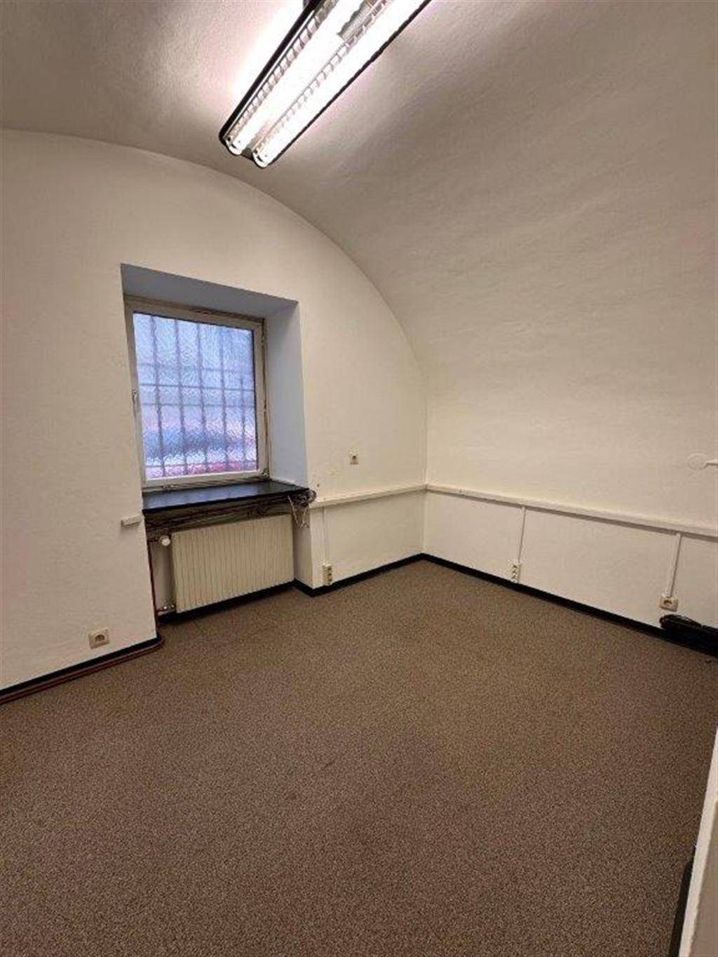 Raum mit gewölbter Decke, Teppichboden und einem Fenster mit Gitterstäben und Heizkörper darunter.
