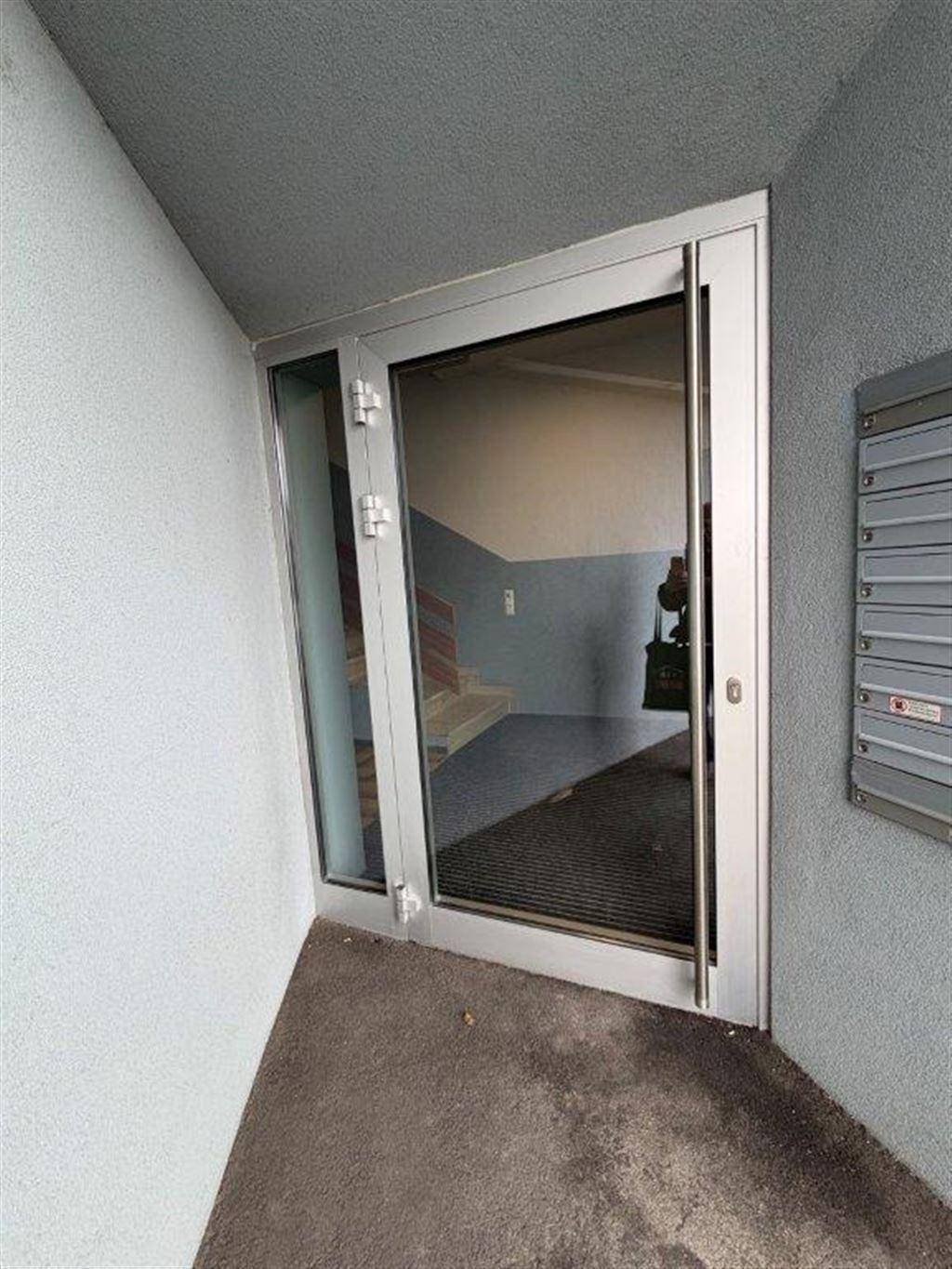 Eingangsbereich mit einer modernen Glastür und Briefkästen, die zu einem Treppenhaus führt.