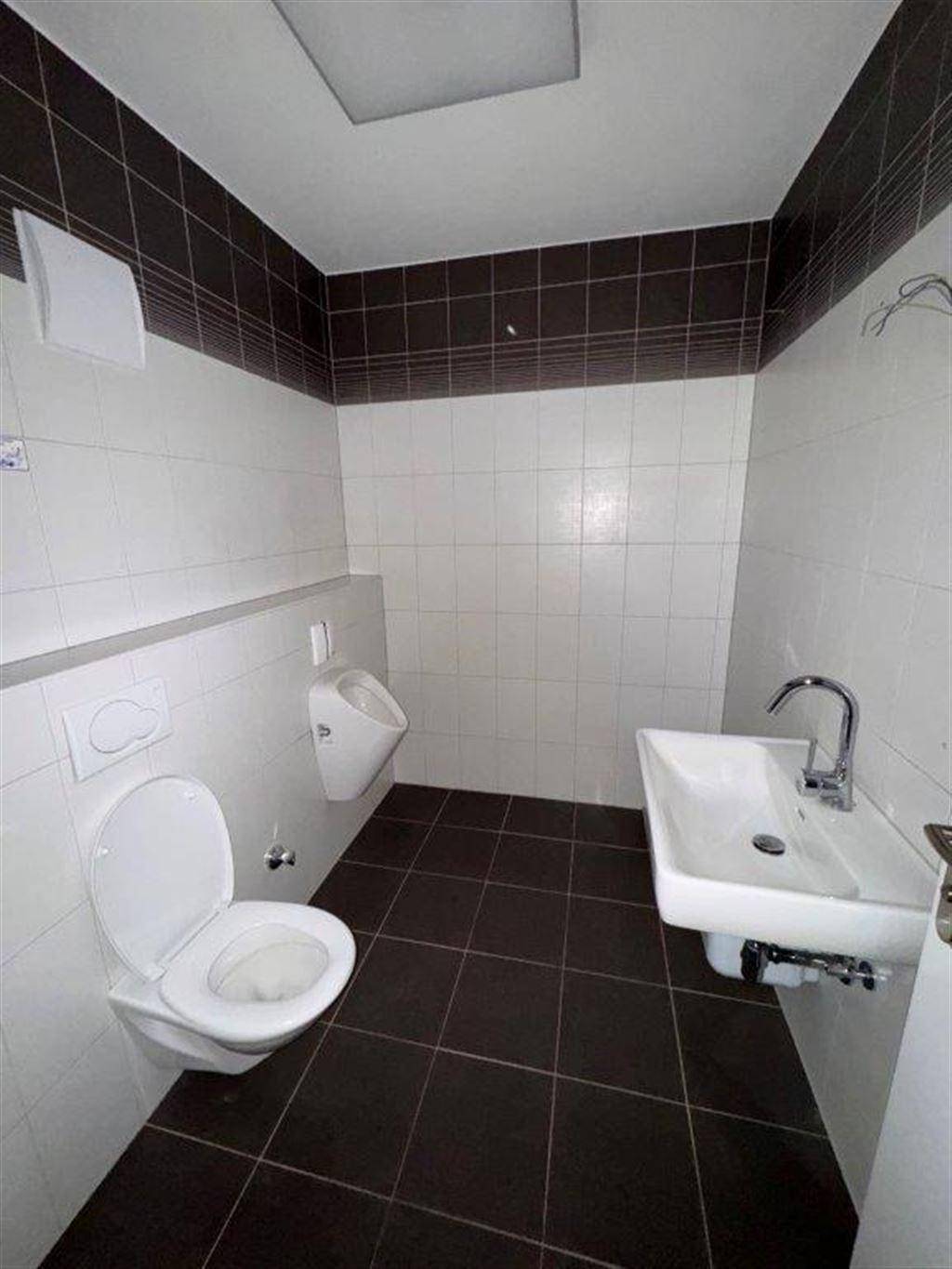 Modern geflieste Gästetoilette mit Urinal, Wand-WC und Waschbecken in dunklen und hellen Tönen.