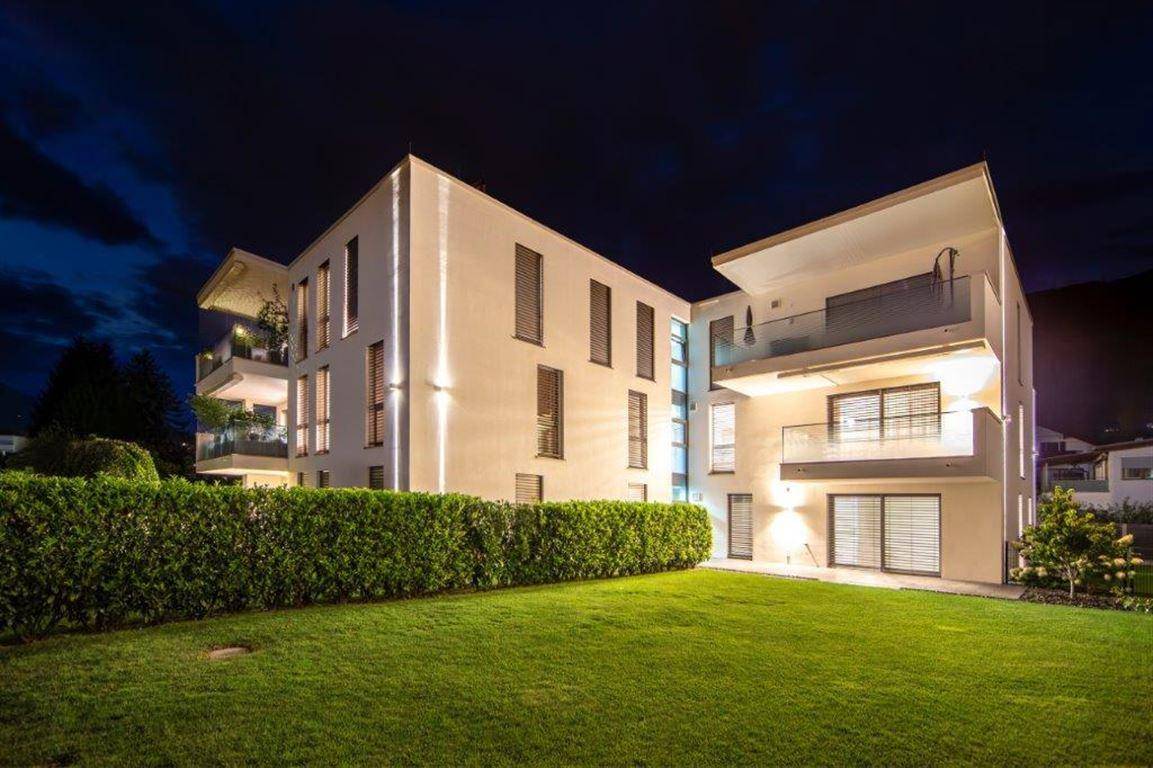 Moderne Wohnanlage bei Nacht mit beleuchteter Fassade und gepflegtem Rasenbereich.