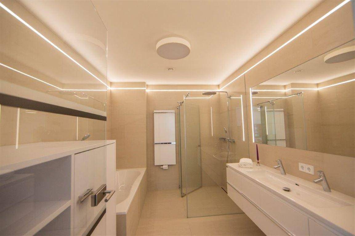 Modernes Badezimmer mit Doppelwaschbecken, Badewanne, Dusche und indirekter Beleuchtung.