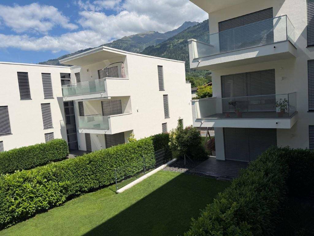 Mehrfamilienhaus mit modernen Balkonen und Blick auf die umliegende Berglandschaft.